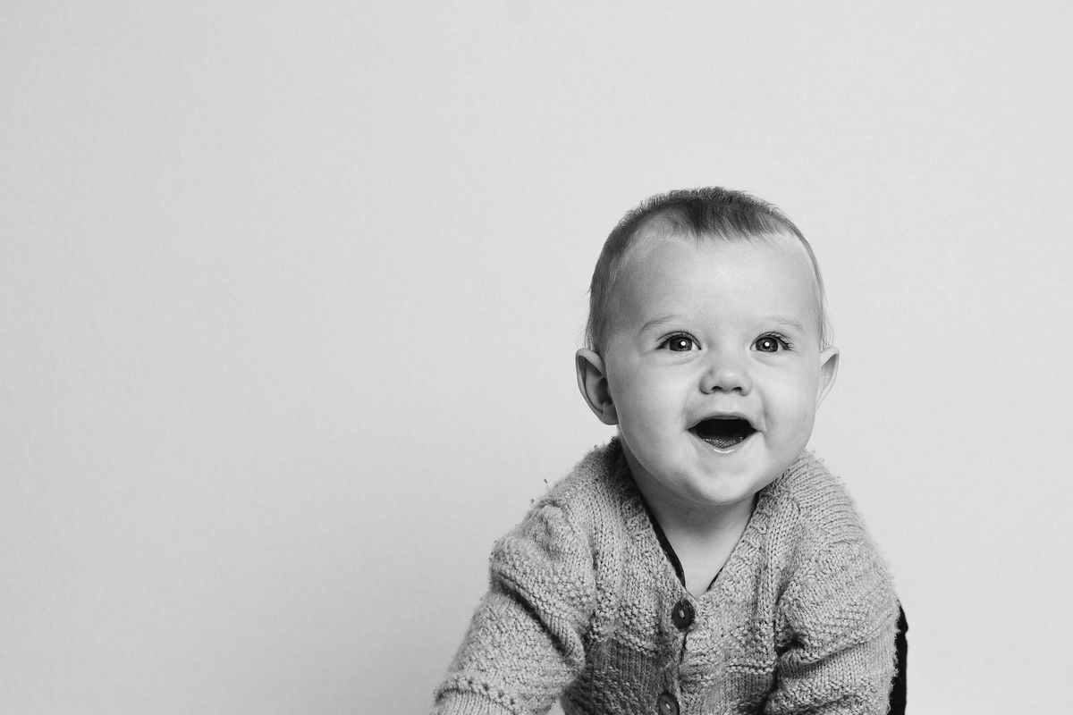 A laughing baby in a knitted cardigan, black and white studio portrait