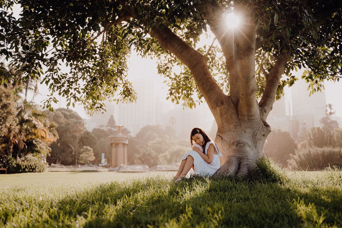 A woman sitting beneath a large tree at golden hour