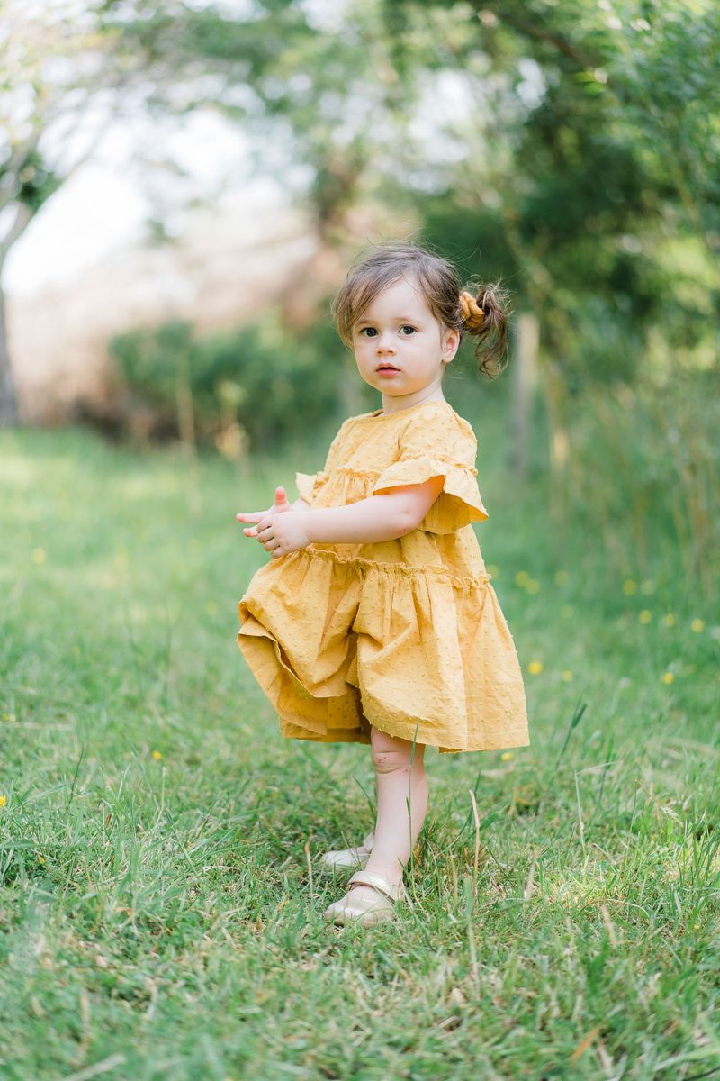 A toddler in a yellow dress in long grass