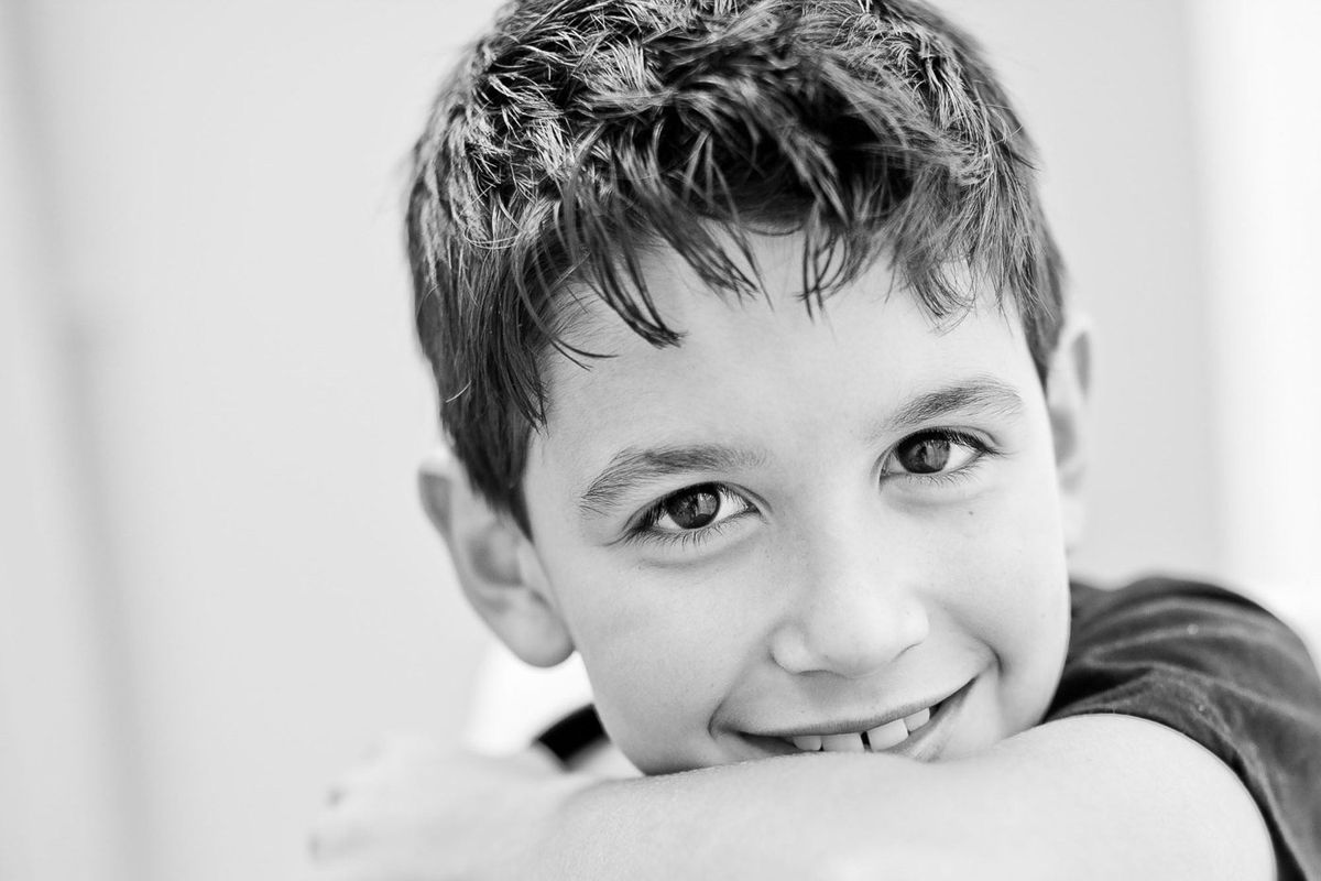 Black and white portrait of a smiling boy resting his chin on his arm