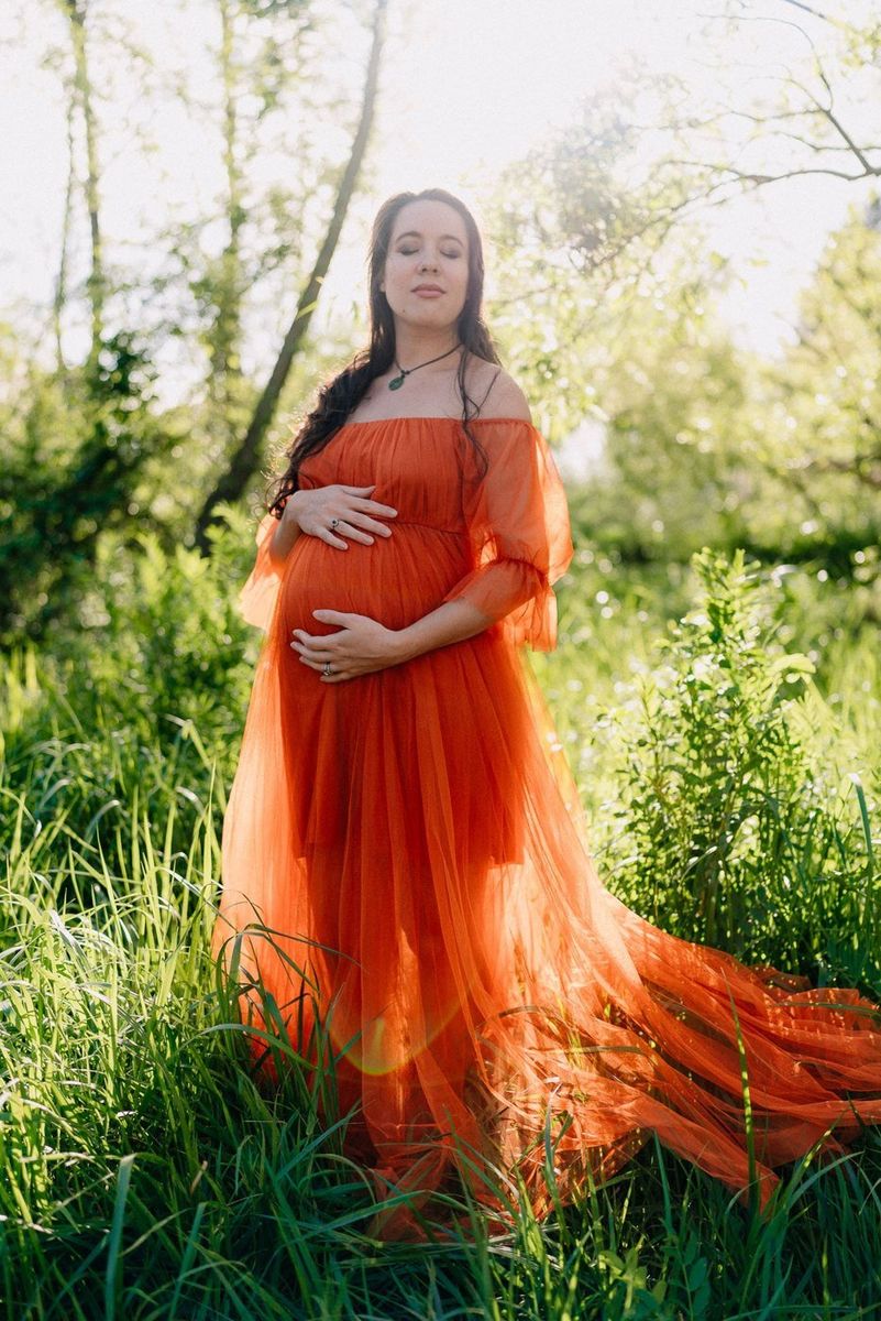A mother-to-be in a flowing red gown in long grass