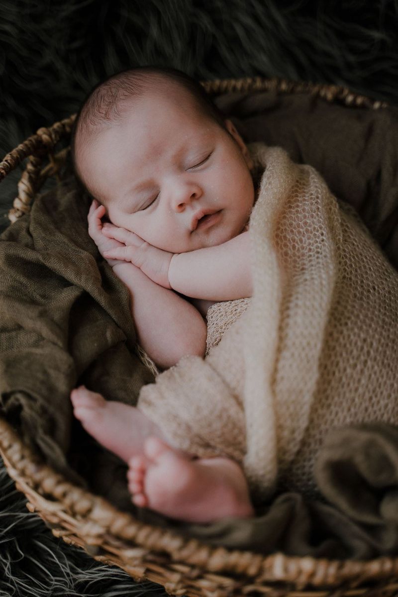 A newborn asleep in a woven basket, wrapped in cream knit